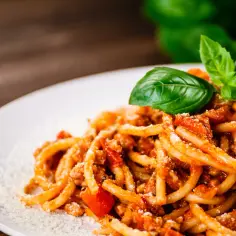 Pyszne spaghetti bolognese, idealne na prosty przepis. Aromatyczny sos mięsny z pomidorami i bazylią, posypany parmezanem.