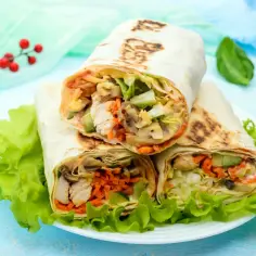 Trzy sycące shoarma drobiowa z kurczakiem, warzywami i grzybami, podane na liściach sałaty.