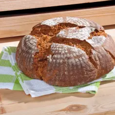 Chleb na drewnianym stole, na zielono-białej ściereczce.