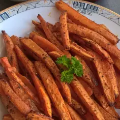Chrupiące, pieczone frytki z marchewki, doprawione ziołami, podane na talerzu z natką pietruszki.