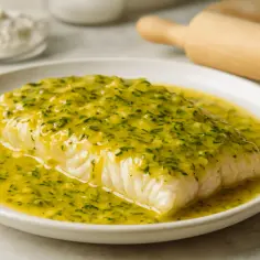 Filet ryby w jasnym sosie cytrynowym z ziołami na białym talerzu.