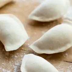 Surowe pierogi bez jajek na drewnianej desce, posypane mąką.
