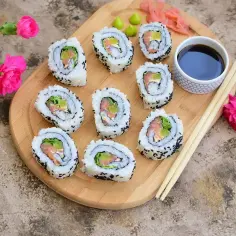 Roladki sushi California Roll z łososiem i awokado na desce, z sosem sojowym i kwiatami.