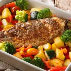 Pieczona ryba z ziemniakami, brokułami i papryką w naczyniu żaroodpornym.