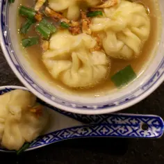 Miseczka zupy wonton z zieloną cebulką i pierożkami na łyżce.