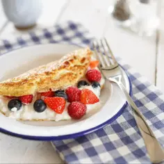 Puszysty omlet z serkiem i owocami leśnymi na talerzu.