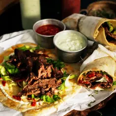 Pyszny lawasz kebab z soczystym mięsem, świeżą sałatą i sosami. Dwa zawinięte tortille i jeden otwarty na desce.