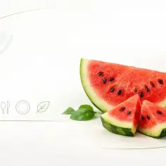 Kawałki soczystego arbuza z pestkami na białym tle, obok ikony serca, sztućców i liścia.