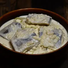 Śledzie w śmietanowym sosie z cebulą w brązowej misce.