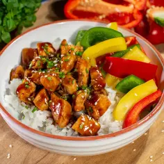 Miseczka ryżu z kurczakiem teriyaki i kolorową papryką, posypana sezamem i szczypiorkiem.