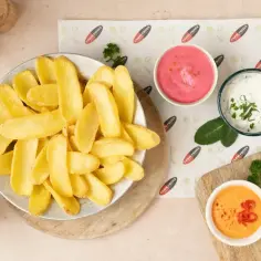 Talerz chrupiących frytek z różowymi, białymi i pomarańczowymi sosami do frytek.