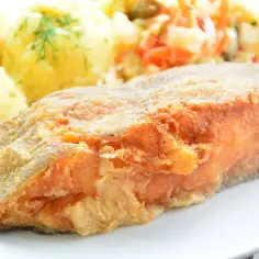 Smażony filet rybny z ziemniakami i surówką na białym talerzu.
