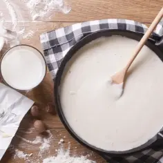 Gładki sos beszamel w patelni, obok mleko, masło i mąka.