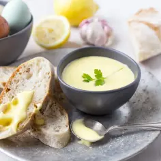 Kremowy sos aioli w miseczce, podany z pieczywem, cytryną i czosnkiem.