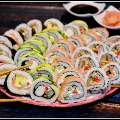Talerz pełen kolorowych uramaki z łososiem, awokado i warzywami. Patyczki do sushi czekają na pierwszy kęs.