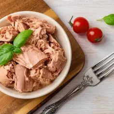 Miseczka tuńczyka w sosie własnym z bazylią, pomidorkami i widelcem.