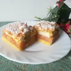Dwa kawałki szarlotki z bezą i kruszonką, posypane cukrem pudrem, na białym talerzu.
