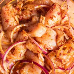 Kawałki kurczaka w misce, gotowe do grillowania. Marynata do kurczaka na grilla z cebulą i przyprawami.