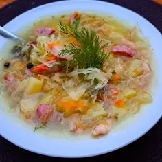 Talerz z kapuśniakiem z kiszonej kapusty, ziemniakami, kiełbasą i koperkiem.