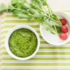 Pesto z liści rzodkiewki, świeże rzodkiewki i zielone liście na zielono-białym tle.