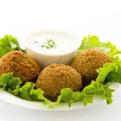 Trzy chrupiące kulki falafel kebab na liściach sałaty, obok miseczki z białym sosem.
