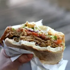 Ręka trzyma pysznego kebaba z mięsem, warzywami i chrupiącą surówką do kebaba.