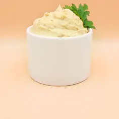 Kremowy hummus w białej miseczce, udekorowany natką pietruszki.