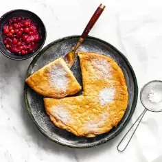 Omlet z cukrem pudrem i żurawiną na talerzu, obok sitko z cukrem.