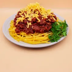 Prosty przepis na spaghetti z mięsem mielonym: makaron z sosem bolońskim, posypany startym serem i udekorowany natką pietruszki.