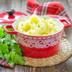 Purée ziemniaczane w czerwonej misce, ozdobione natką pietruszki, na drewnianym stole.