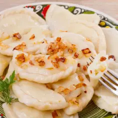 Pyszne pierogi ruskie z farszem Magdy Gessler, posypane skwarkami, na ozdobnym talerzu.