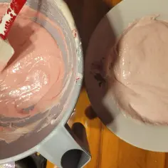 Różowa masa na makaroniki francuskie w misce i na talerzyku. Szpatułka miesza kremową konsystencję.
