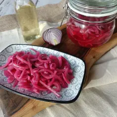 Marynowana czerwona cebula na talerzyku, w słoiku i połówka cebuli obok.