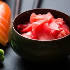 Miseczka z marynowanym imbirem, obok sushi z łososiem i wasabi.