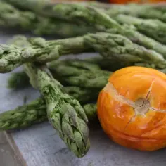 Zielone szparagi i pomarańczowy pomidor na drewnianym tle.