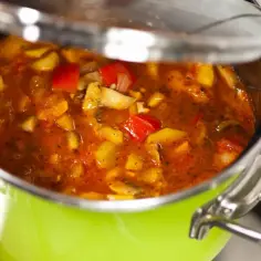 Gęste leczo z papryką i ziemniakami gotujące się w zielonym garnku pod lekko uchyloną pokrywką.
