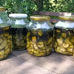 Pięć słoików z nalewką z orzecha włoskiego, przygotowaną z zielonych, pokrojonych owoców, stoi na drewnianym stole.