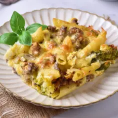 Zapiekanka makaronowa z mięsem mielonym i brokułami, posypana serem, na talerzu z bazylią.