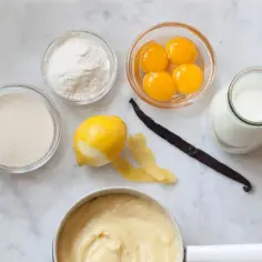 Składniki do kremu patissiere: żółtka, cukier, mąka, mleko, cytryna, laska wanilii i gotowy krem.