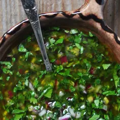 Sos chimichurri w glinianej misce z łyżką, pełen ziół i czerwonej cebuli.