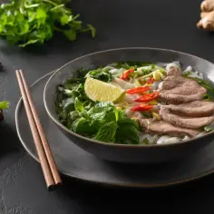 Aromatyczne pho z wołowiną, makaronem ryżowym, świeżą miętą, kolendrą, chili i limonką. Obok pałeczki i przyprawy.