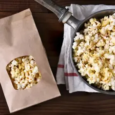 Popcorn w garnku i papierowej torbie na drewnianym tle.