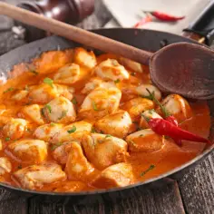 Pyszne co na obiad z piersi kurczaka w kremowym sosie, ozdobione papryczkami chili i drewnianą łyżką.