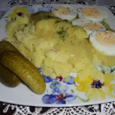 Talerz z ziemniakami, jajkami na twardo, ogórkami kiszonymi i sosem musztardowym.