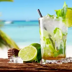 Szklanka orzeźwiającego mojito z limonką i miętą na tle plaży.