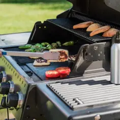 Ręka z szczypcami obraca na grillu pyszne halloumi z grilla, obok pieczone pomidory i papryczki.