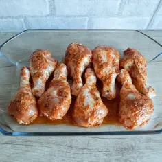 Gotowe do pieczenia pałki z kurczaka, doprawione i ułożone w szklanym naczyniu.
