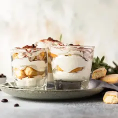 Pyszny włoski deser tiramisu w szklankach, udekorowany kakao i kawą.