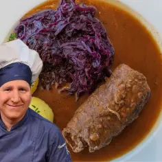 Szef kuchni prezentuje pyszne danie: roladę śląską z modrą kapustą i kluskami ziemniaczanymi w sosie.