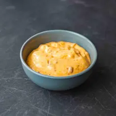 Pomarańczowy sos chipotle w niebieskiej miseczce na ciemnym tle.